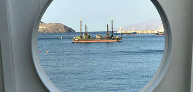 Blick durch ein Rundfenster einer Fähre auf ein anderes Boot und Land im Hintergrund