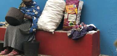 Frau sitzt auf einer Bank, neben ihr Säcke