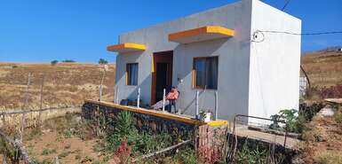 Weißes Haus mit Person davor in einer kargen Landschaft