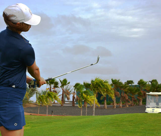 Golferin im blauen Outfit, im Hintergrund fährt ein Golfcaddy