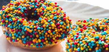 Zwei Donuts auf einem Teller mit Schokoüberzug und bunten runden Streuseln