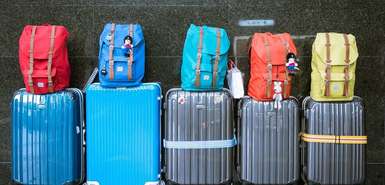 Blaue und graue Koffer mit bunten Rucksäcken oben drauf